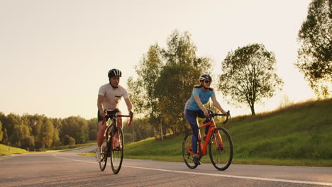 Steadicam-shot-of-two-healthy-mem-and-woman-peddling-fast-with-cycling-road-bicycle-at-sunset